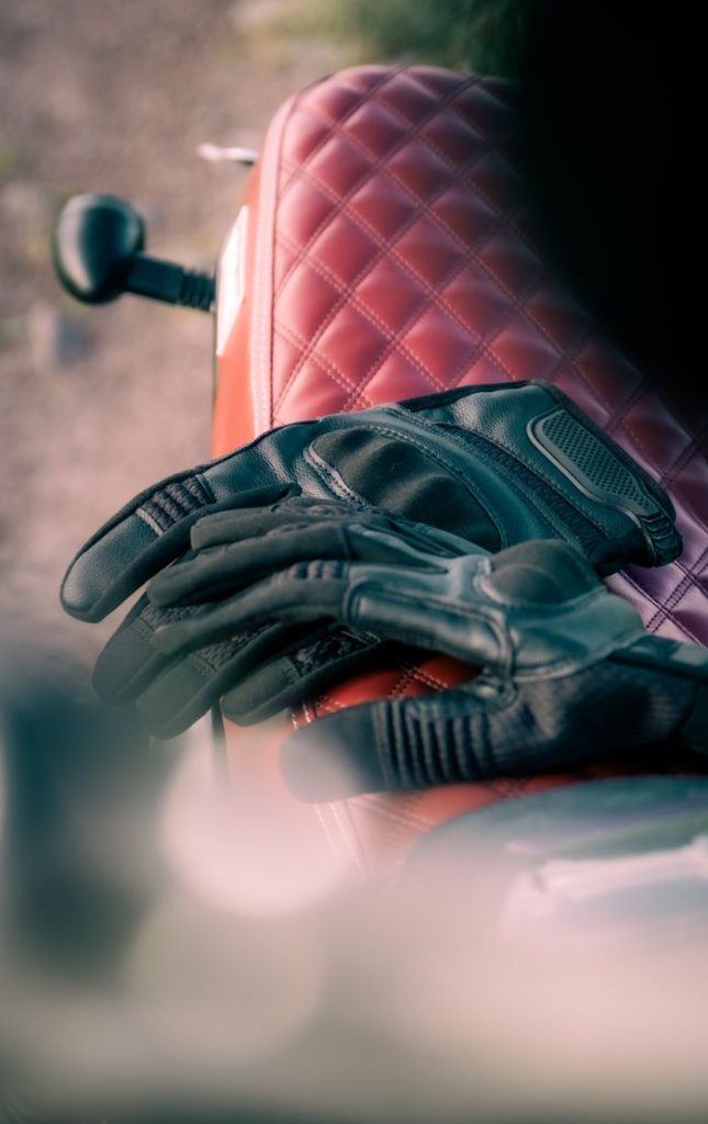 Black leather gloves on a quilted motorcycle seat, emphasizing style and adventure.