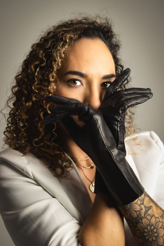 A fashionable woman poses with black leather gloves in a studio setting, highlighting style and elegance.