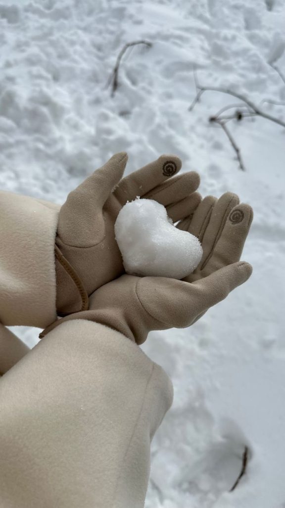 Heart-shaped snowball in gloved hands, capturing the essence of a serene winter day.