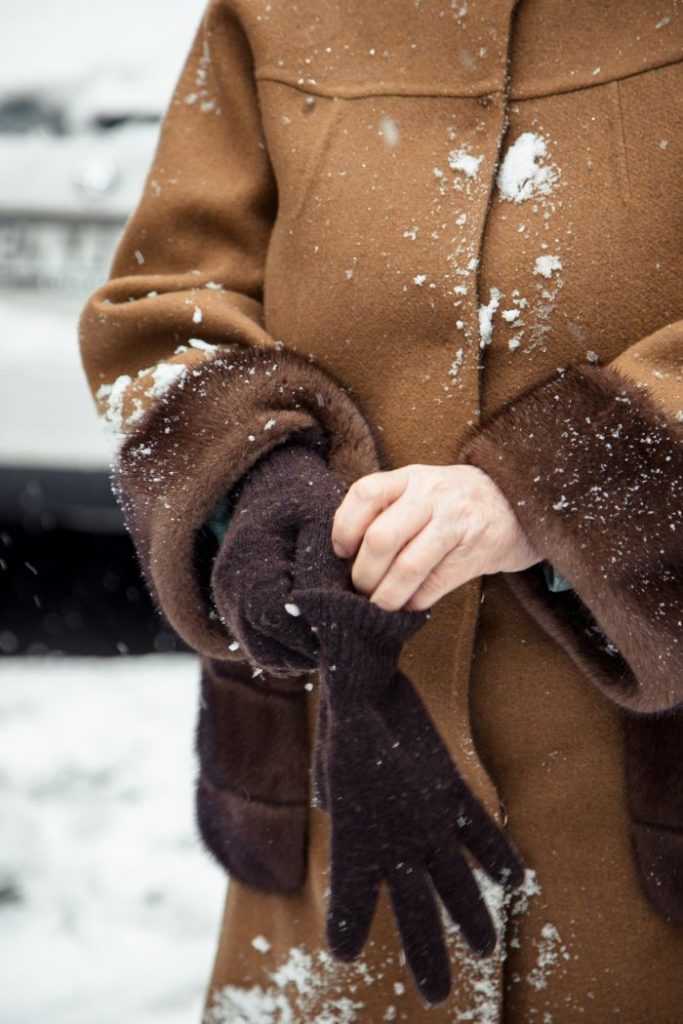 Crop unrecognizable woman in warm coat wearing mittens on snowy street in winter time in daylight