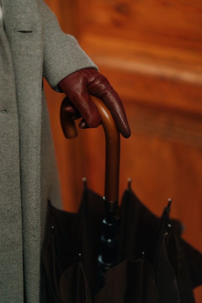 Close-up of a hand in a leather glove holding an umbrella against a wooden door background.